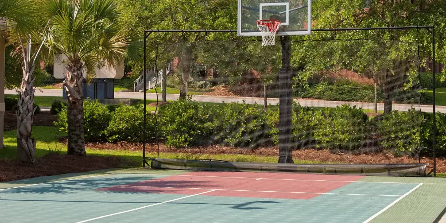 Outdoor basketball court with a netted enclosure, surrounded by greenery and palm trees.