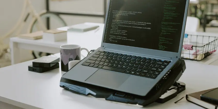 A laptop on a portable stand, displaying code on the screen, set in a modern office space with coffee and notebooks.
