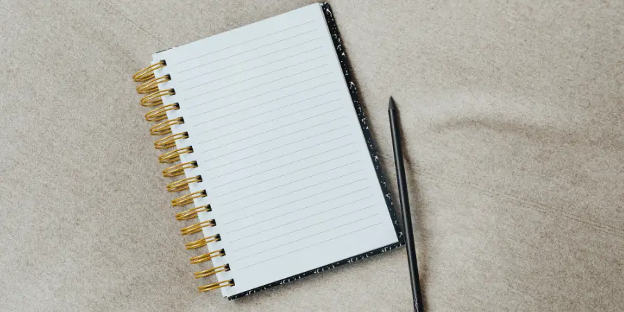 An open spiral notepad with lined pages placed beside a black pen.