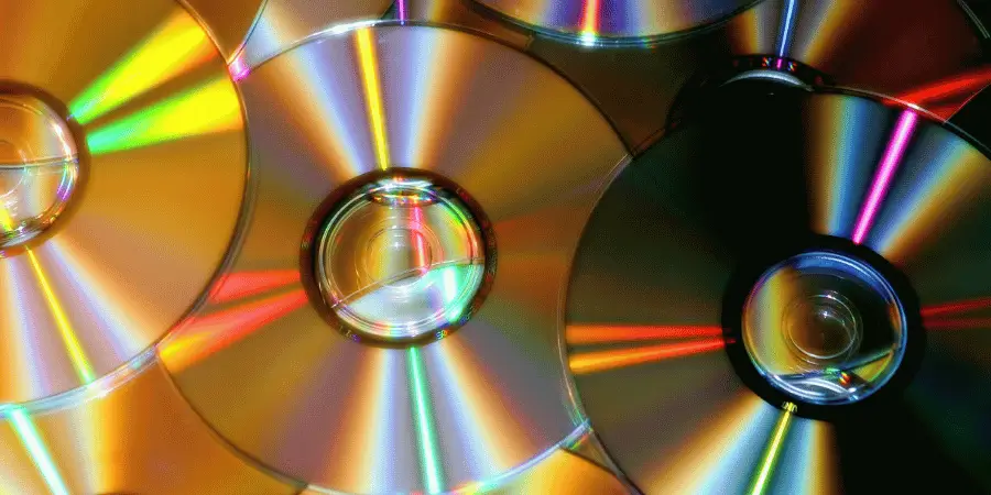 A collection of shiny CDs overlapping and reflecting rainbow light.