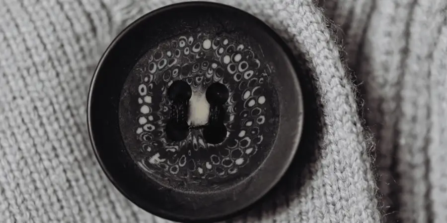A close-up of a black button sewn onto textured gray fabric.