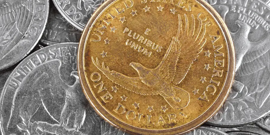 A close-up of a gold U.S. dollar coin lying on top of several silver quarters.