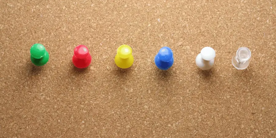 A row of colorful push pins lined up on a corkboard surface.
